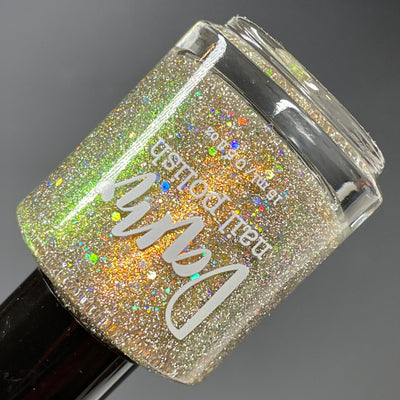 Sunny Side Up by Dam Nail Polish, gold-to-green shifting shimmer with silver holographic and reflective glitter under studio light, bottle standalone product shot