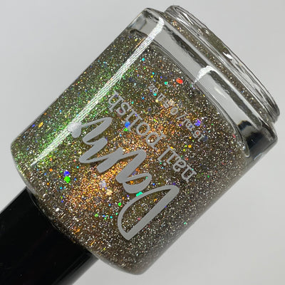 Sunny Side Up by Dam Nail Polish, dual bottle standalone product shot comparing warmer gold studio tone left to silver-green flash-activated glitter scatter right