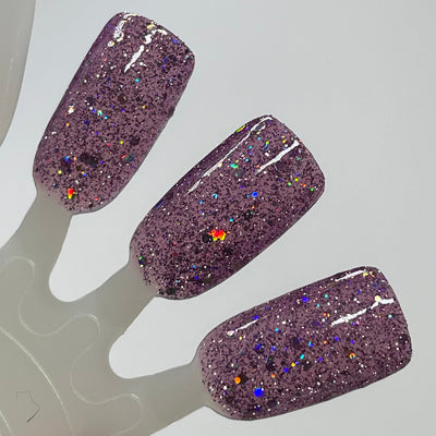Thistle be the Day by Dam Nail Polish, warm dusty mauve-purple jelly with silver micro-glitter and chunky holographic flakes showing vivid rainbow scatter under studio light, swatch stick