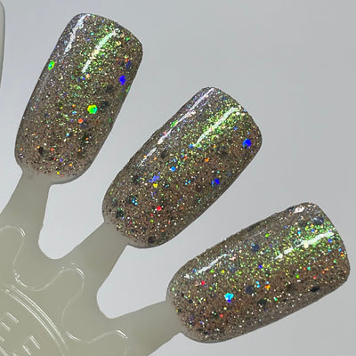 Thyme to Shine by Dam Nail Polish, warm taupe-greige base with green-to-gold shimmer shift, mixed fine micro-glitter and multicolour hex-cut holographic flakes under direct flash, swatch stick