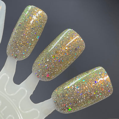 Sunny Side Up by Dam Nail Polish, gold-green shifting shimmer with rainbow holographic glitter scatter under studio light, swatch stick