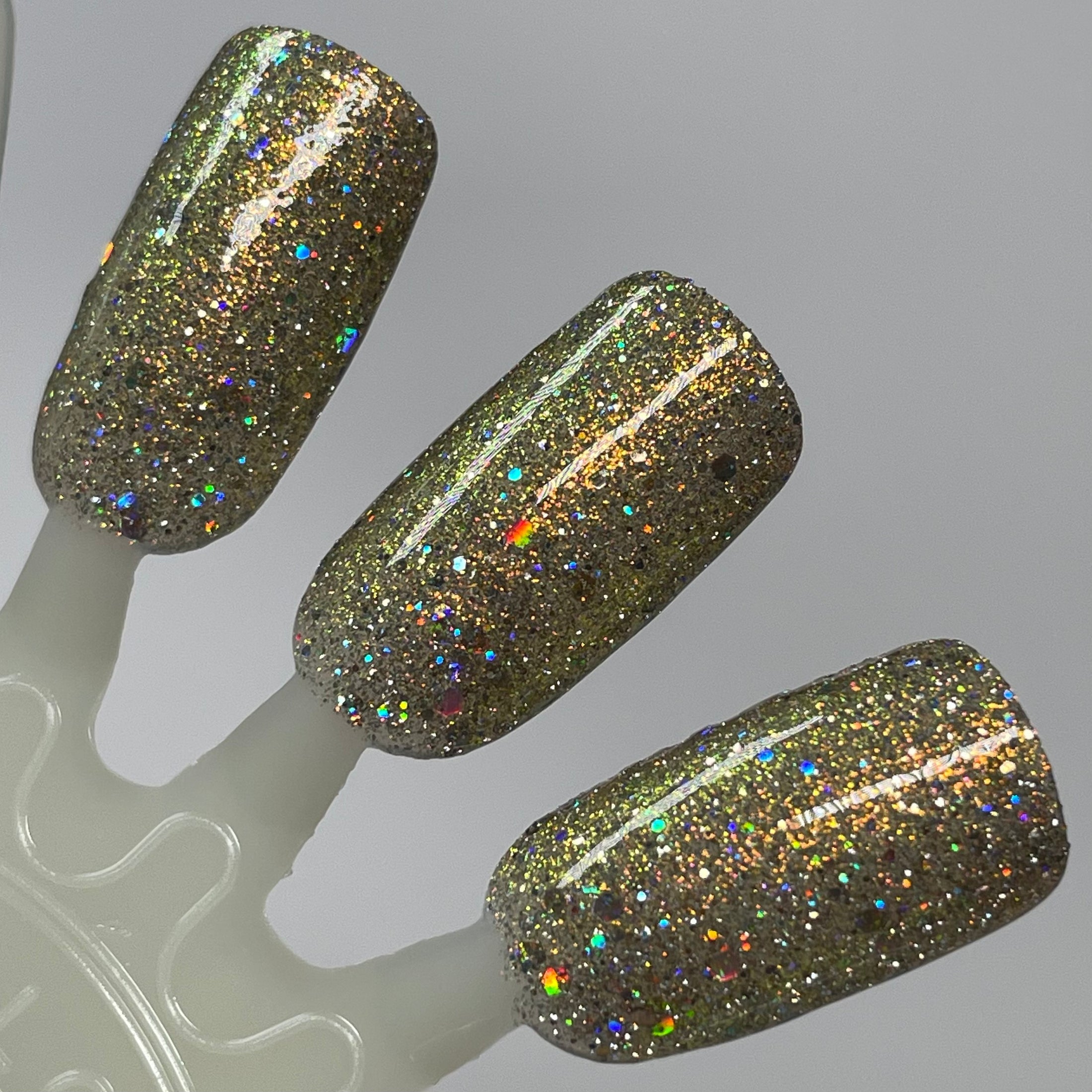 Sunny Side Up by Dam Nail Polish, olive-gold base with dense scattered hex and silver holo reflective glitter under direct flash, swatch stick