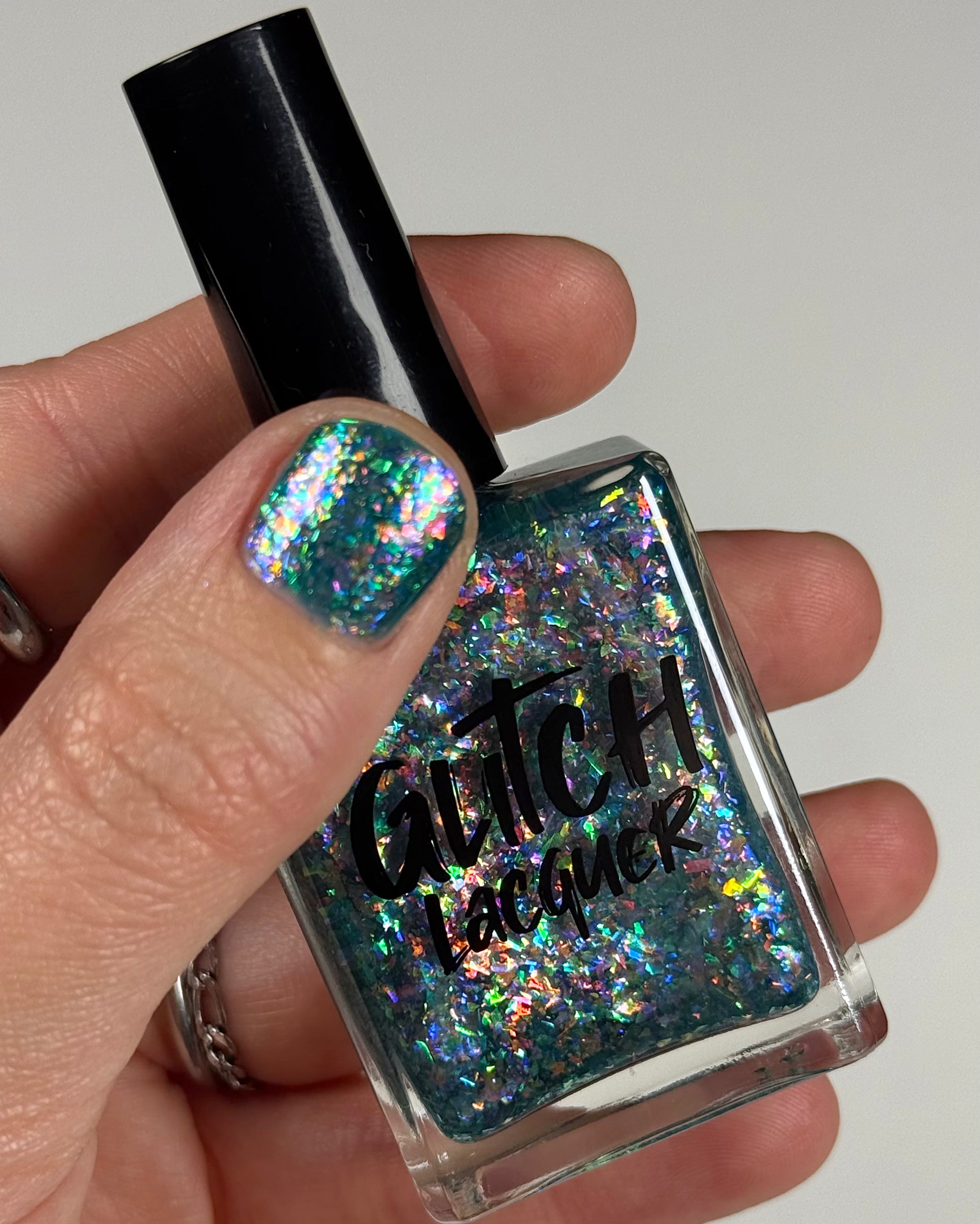 Medo by Glitch Lacquer, teal jelly with iridescent flakies bottle in hand, light-medium skin