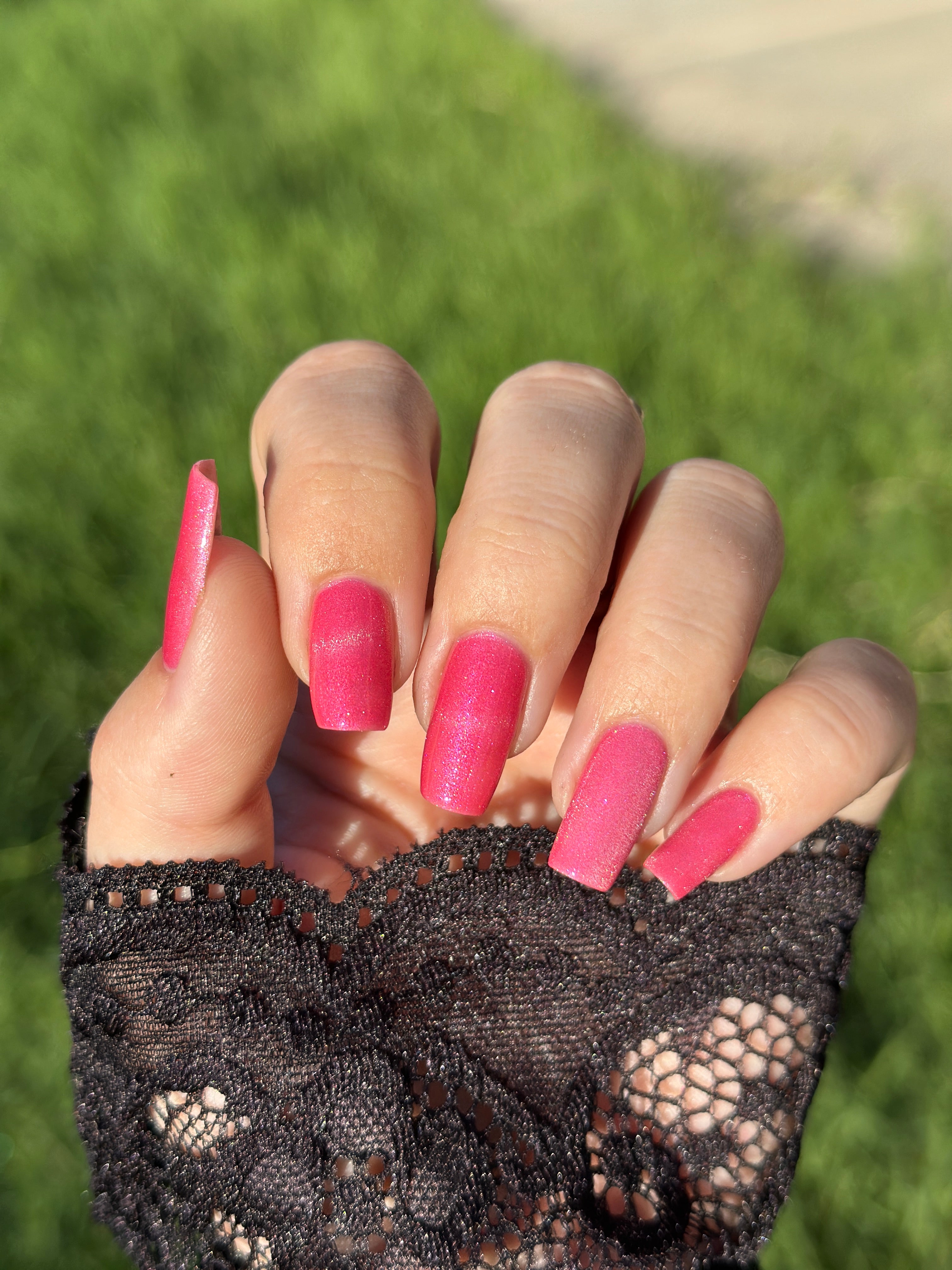 Lovey Dovey by Glitch Lacquer on five long square nails worn with a black lace glove, warm pink polish with pink-to-gold reflective shimmer, light-medium skin tone, bright daylight.