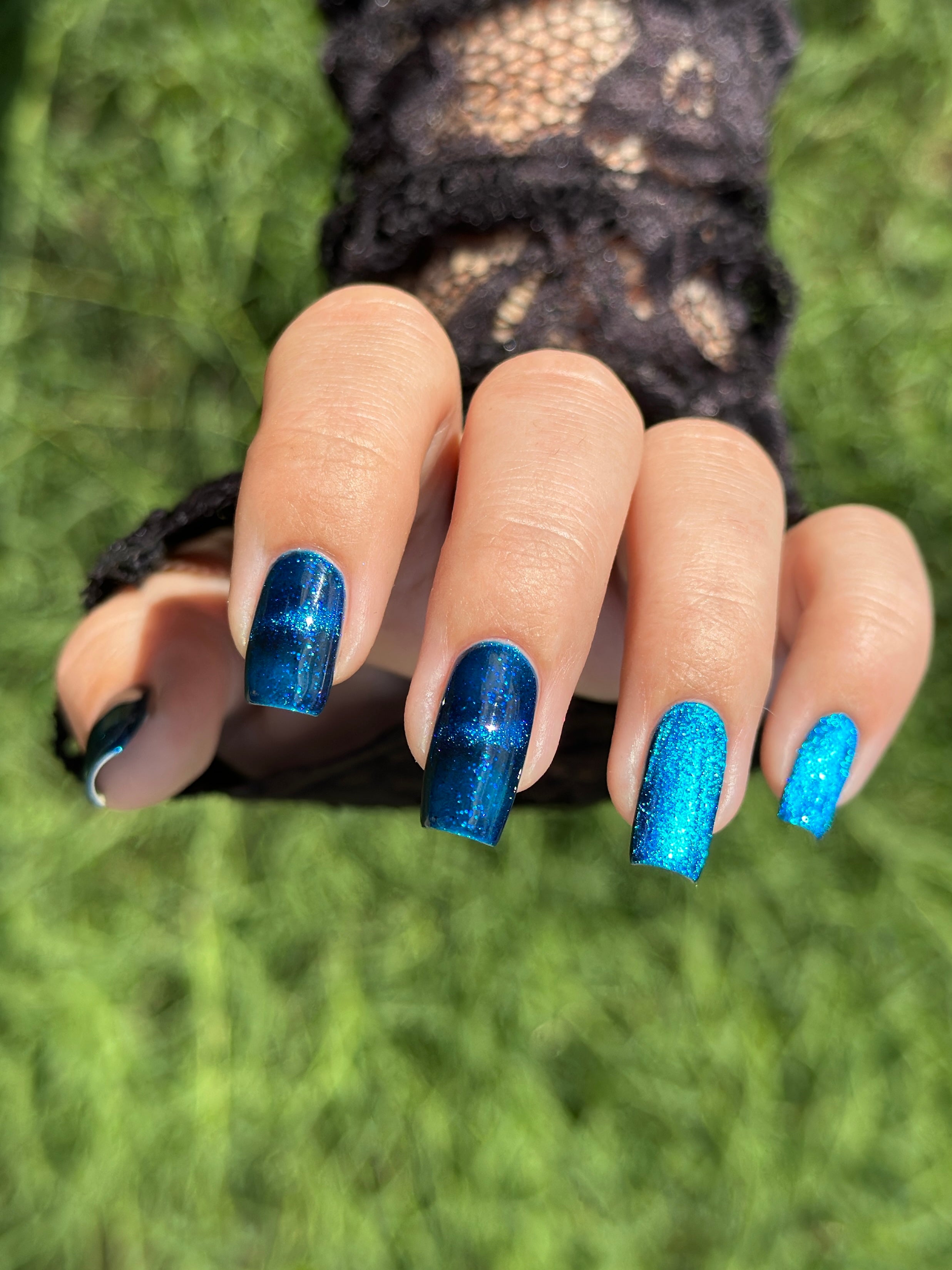 Heart of the Ocean by Glitch Lacquer on five mixed-shape nails, deep blue magnetic jelly with blue-to-purple shift and blue glitters, light-medium skin tone, bright daylight.