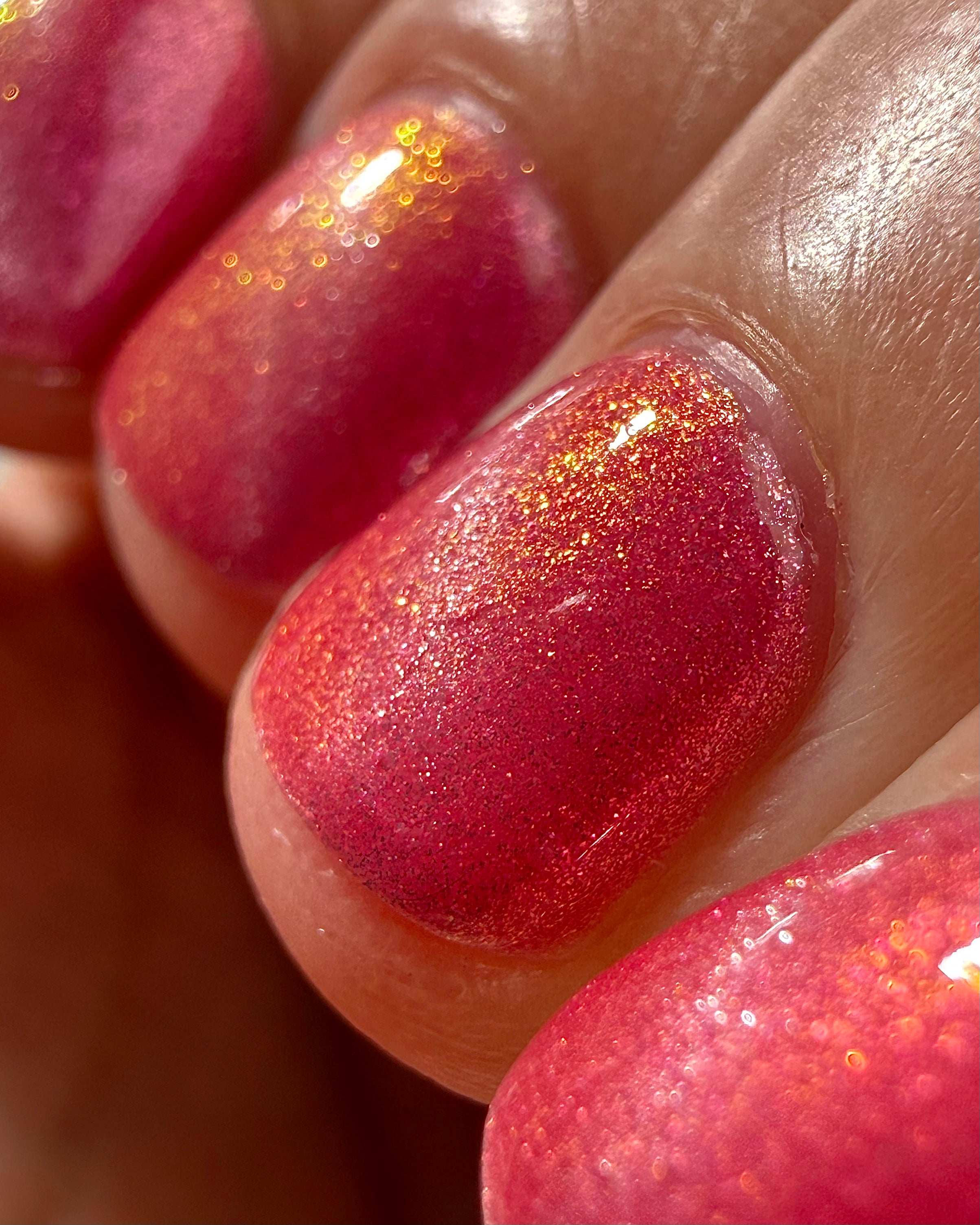 Lovey Dovey by Glitch Lacquer macro detail on four nails showing the silver magnetic line, warm pink polish with strong pink-to-gold reflective shimmer, light-medium skin tone, bright daylight.
