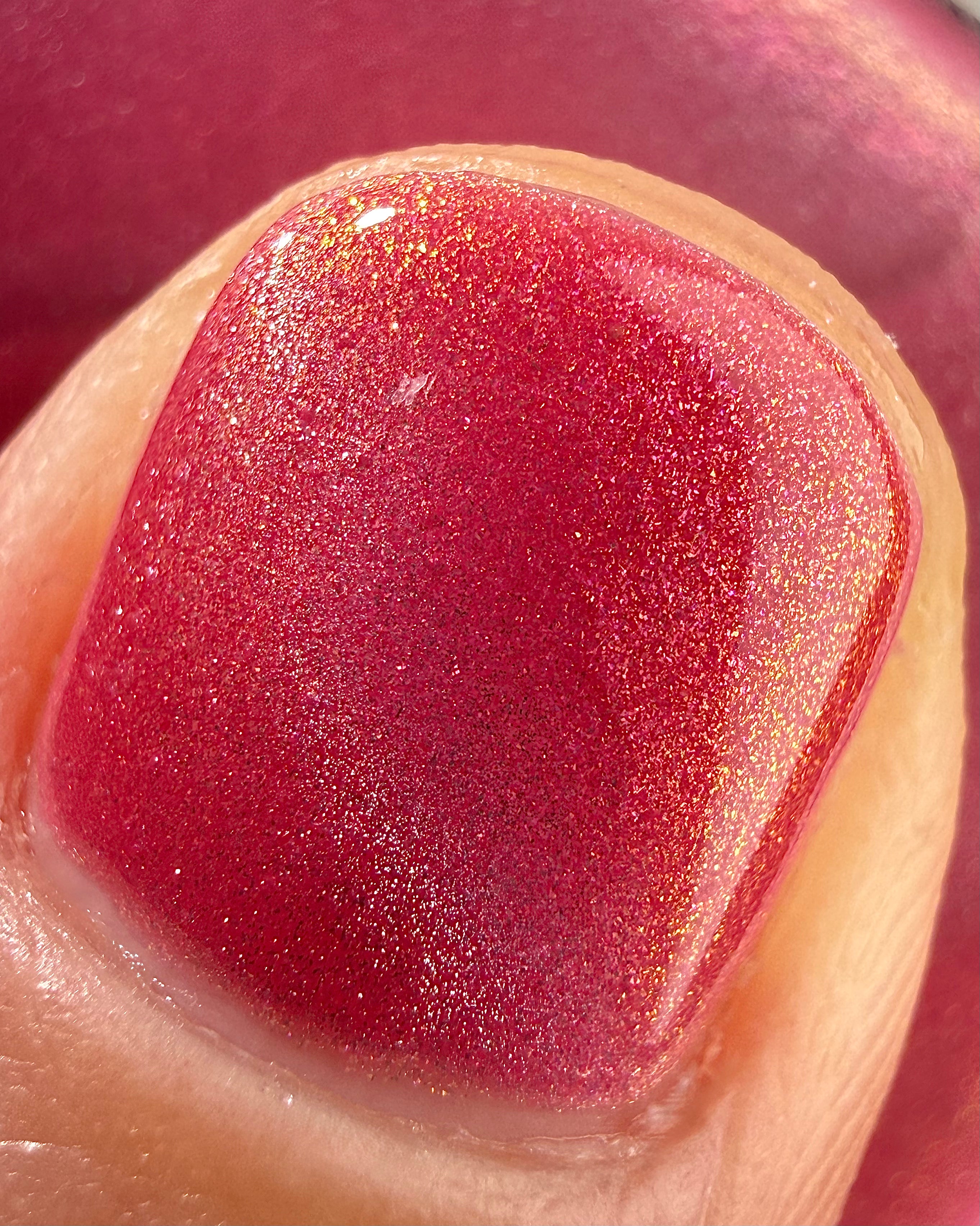Lovey Dovey by Glitch Lacquer macro detail on a single nail, warm pink polish with strong pink-to-gold reflective shimmer, light-medium skin tone, bright daylight.