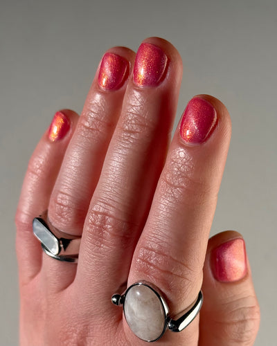 Lovey Dovey by Glitch Lacquer on five short natural round nails, warm pink polish with pink-to-gold reflective shimmer and silver magnetic pigment, light skin tone, bright daylight.