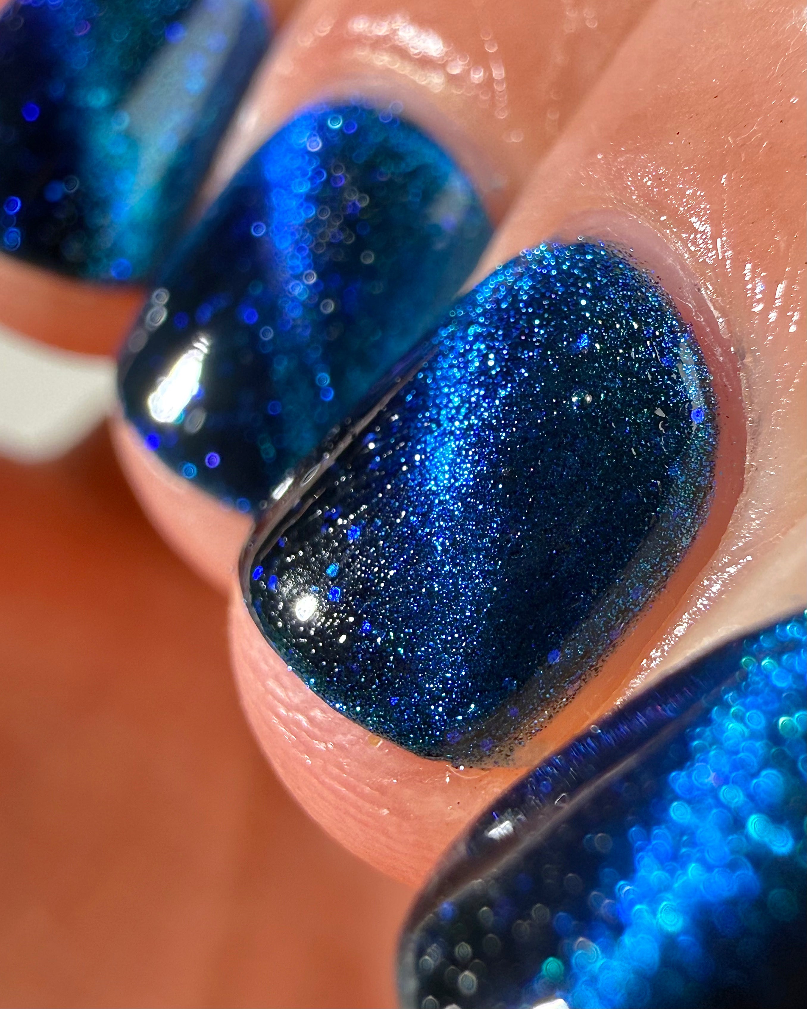 Heart of the Ocean by Glitch Lacquer macro detail showing deep blue jelly with magnetic blue-to-purple shimmer and blue glitters, light skin tone, studio lighting.