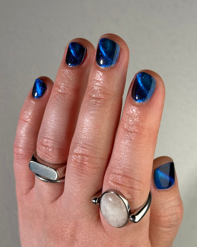Heart of the Ocean by Glitch Lacquer on five short natural nails, deep blue magnetic jelly with blue glitters, light skin tone, studio lighting.