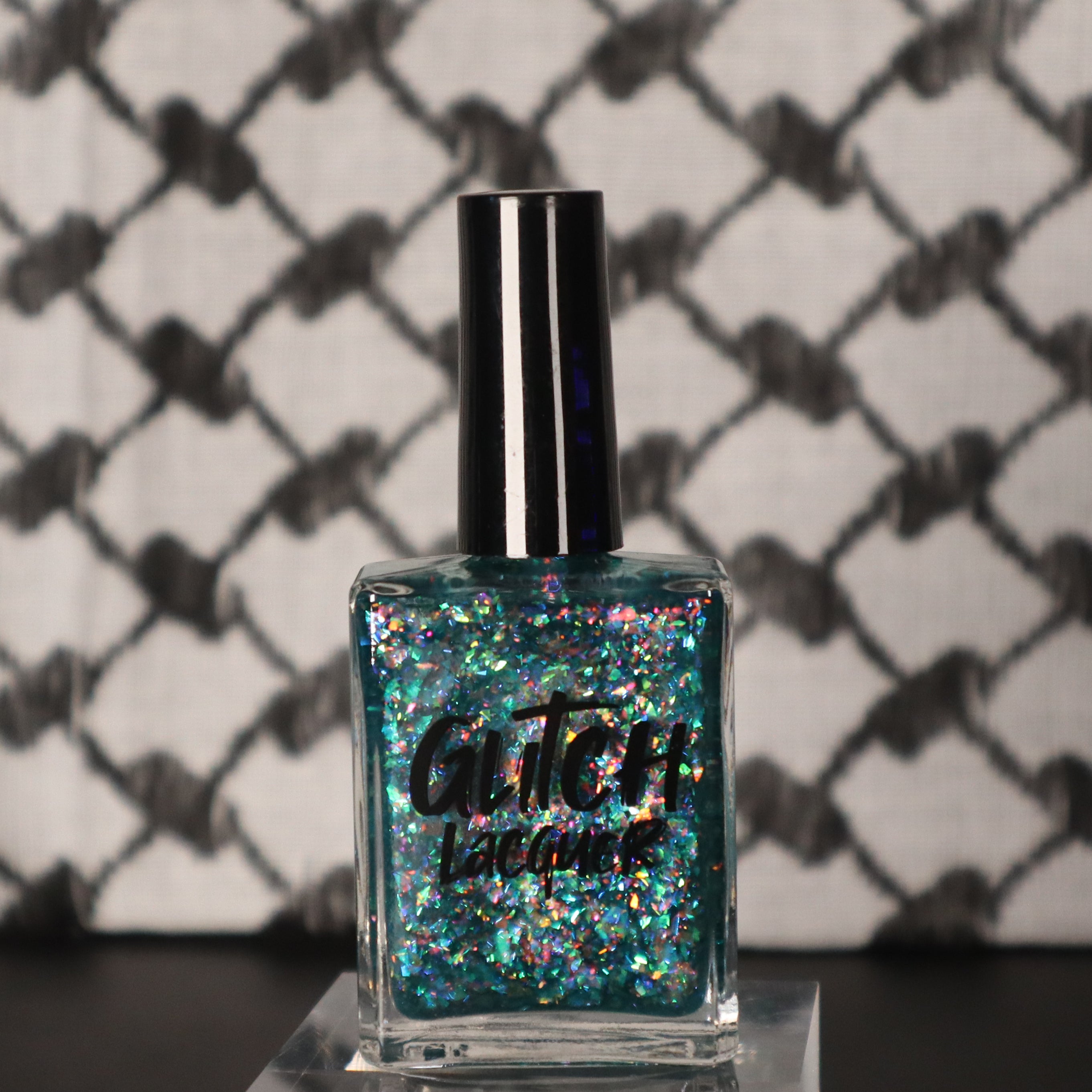 Medo by Glitch Lacquer, teal jelly with iridescent flakies bottle on keffiyeh-patterned background