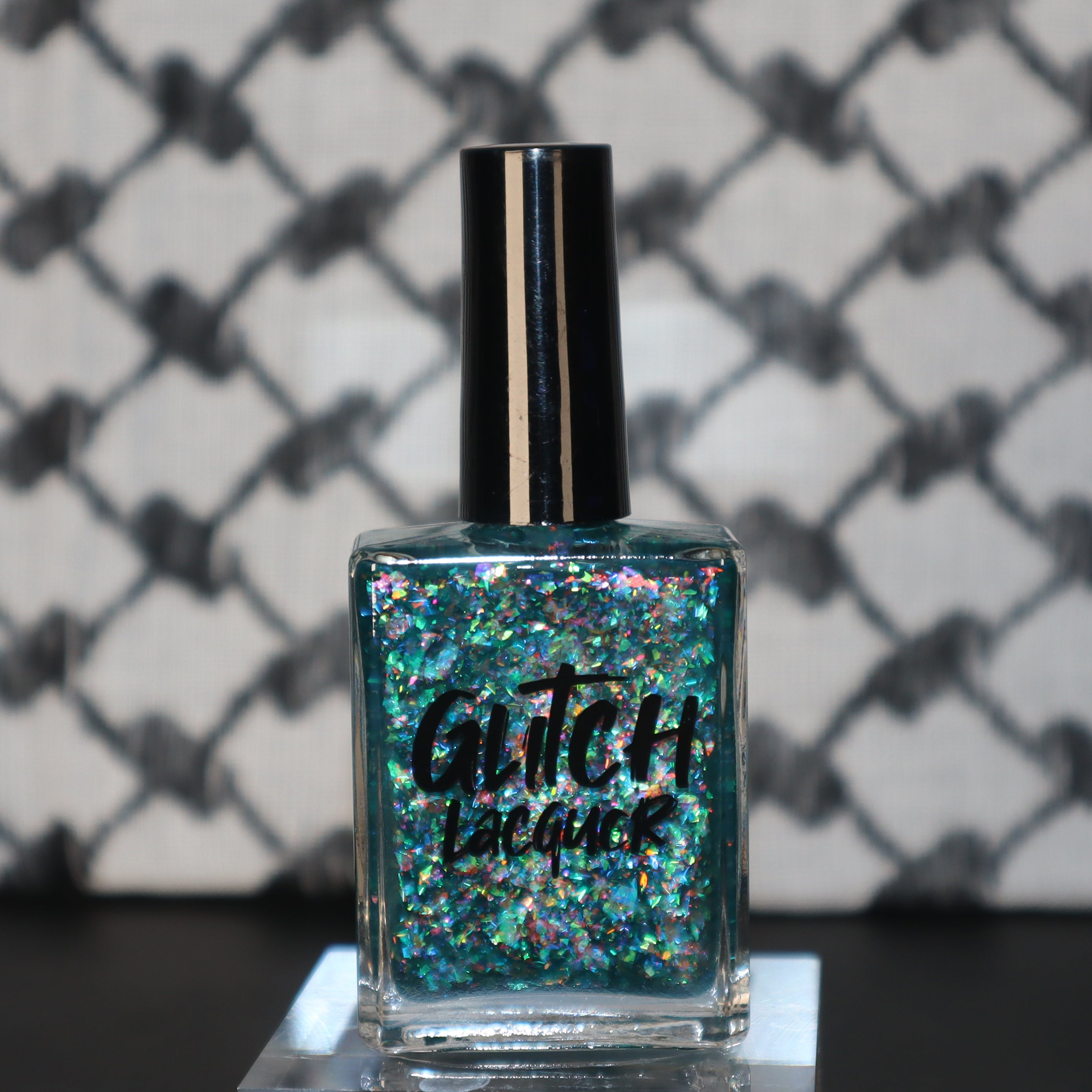 Medo by Glitch Lacquer, teal jelly with iridescent flakies bottle on keffiyeh-patterned background