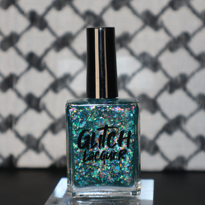 Medo by Glitch Lacquer, teal jelly with iridescent flakies bottle on keffiyeh-patterned background