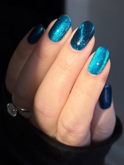 Heart of the Ocean by Glitch Lacquer on five oval nails, deep blue magnetic jelly with blue-to-purple shift and blue glitters, light skin tone, bright studio lighting.