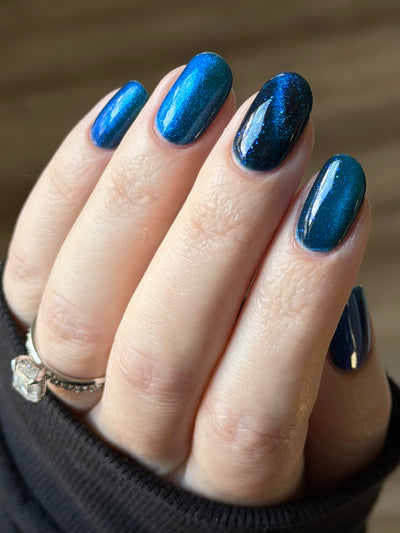 Heart of the Ocean by Glitch Lacquer on five oval nails with a magnetic stripe on the ring finger, deep blue jelly with blue glitters, light skin tone, bright daylight.