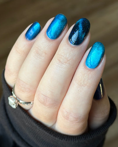 Heart of the Ocean by Glitch Lacquer on four oval nails with a strong magnetic cat-eye on the middle finger, deep blue jelly with blue glitters, light skin tone, bright daylight.