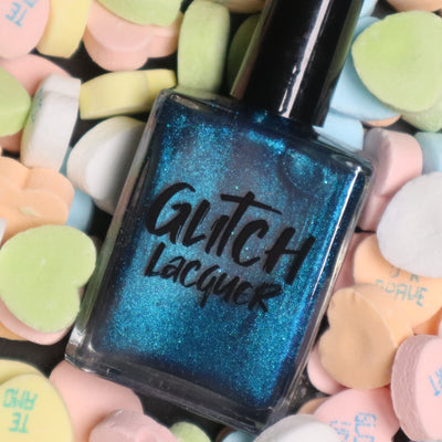 Heart of the Ocean by Glitch Lacquer bottle front shown among pastel heart-shaped candies, deep blue magnetic jelly with blue glitters, studio lighting.
