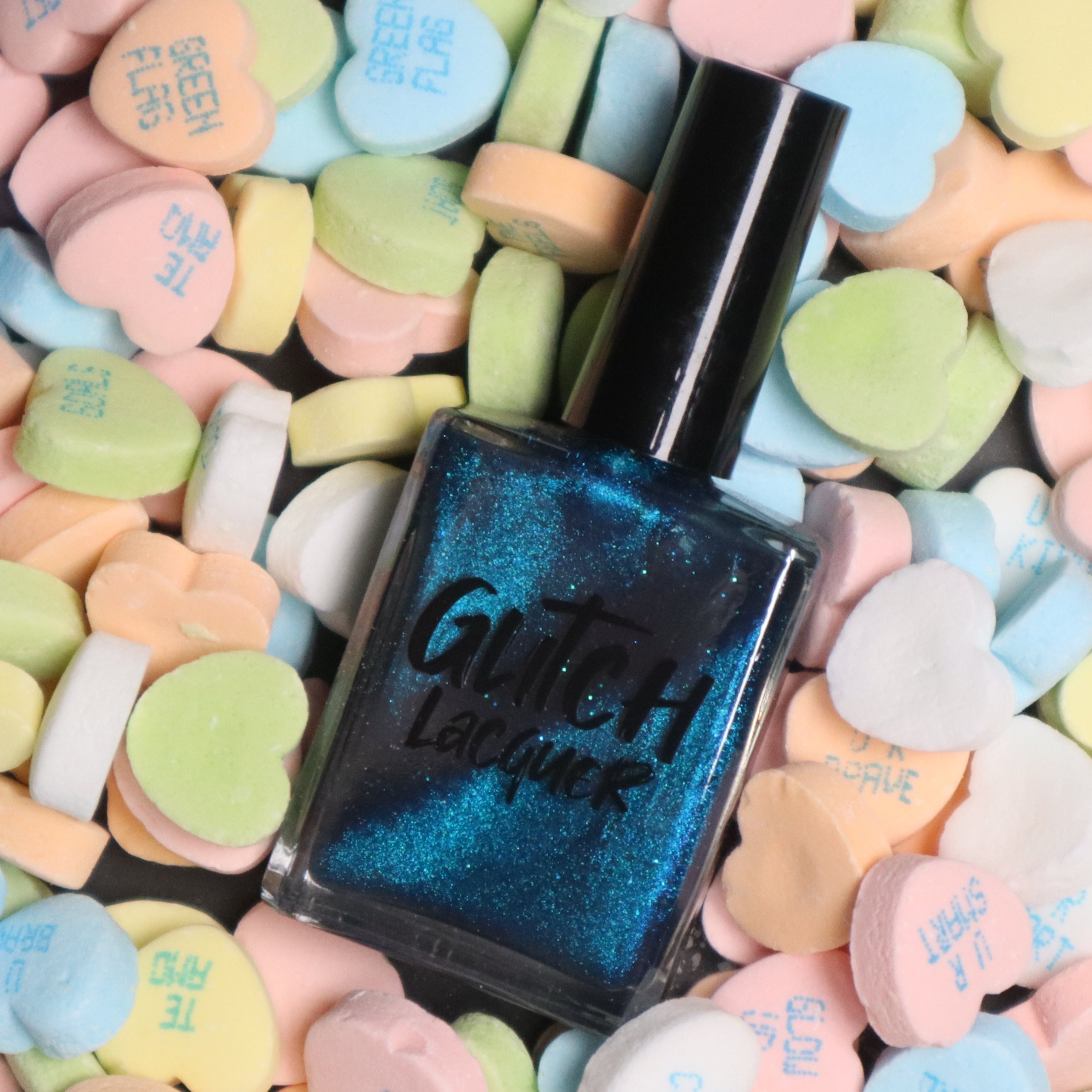 Heart of the Ocean by Glitch Lacquer bottle standing upright on a bed of pastel heart-shaped candies, deep blue magnetic jelly with blue glitters, studio lighting.