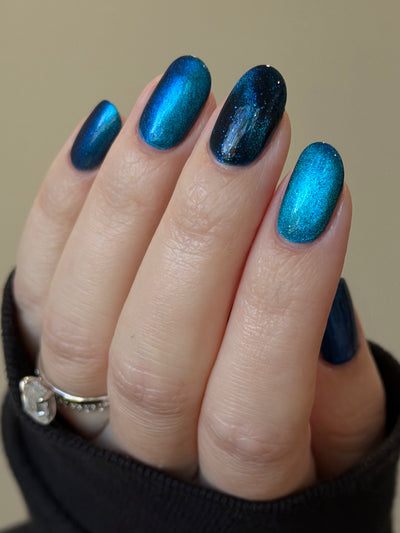 Heart of the Ocean by Glitch Lacquer on five oval nails comparing magnetic and non-magnetic finishes, deep blue jelly with blue glitters, light skin tone, bright daylight.