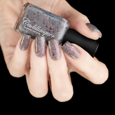Cadillacquer Daydreaming grey red chameleon iridescent crelly nail polish, bottle held with five-nail swatch, light skin, studio lighting