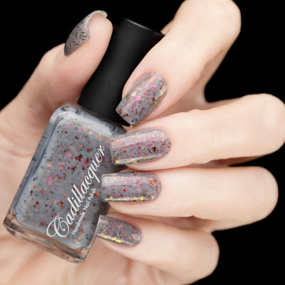 Cadillacquer Daydreaming grey red chameleon iridescent crelly nail polish, bottle held with five-nail swatch, light skin, studio lighting