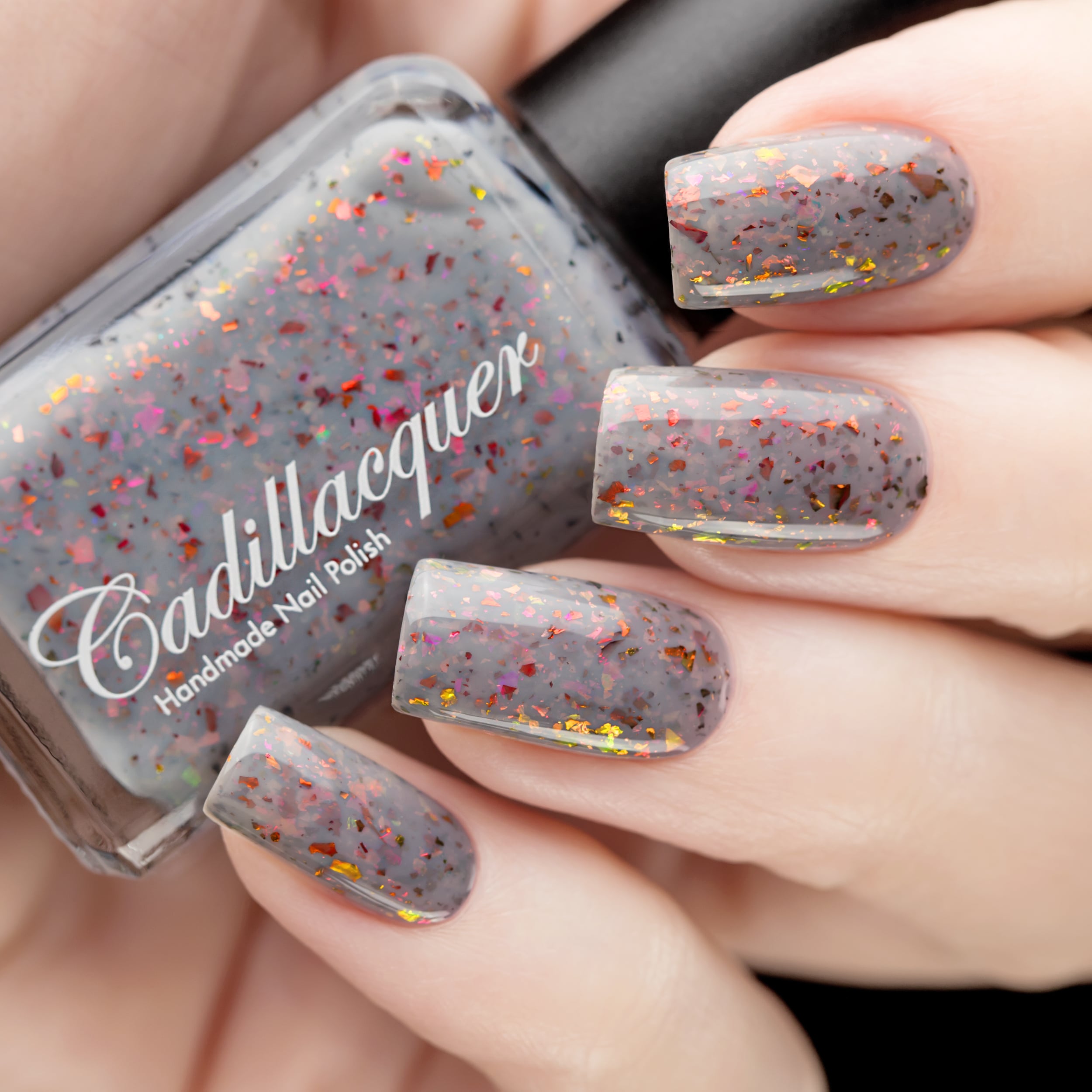 Cadillacquer Daydreaming grey red chameleon iridescent crelly nail polish, bottle held with four-nail swatch, light skin, studio lighting