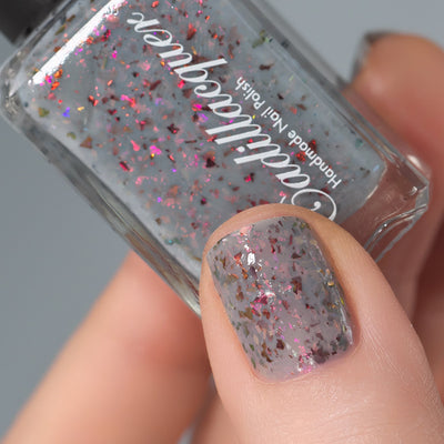 Cadillacquer Daydreaming grey red chameleon iridescent crelly nail polish, bottle held with one-nail swatch, light skin, studio lighting