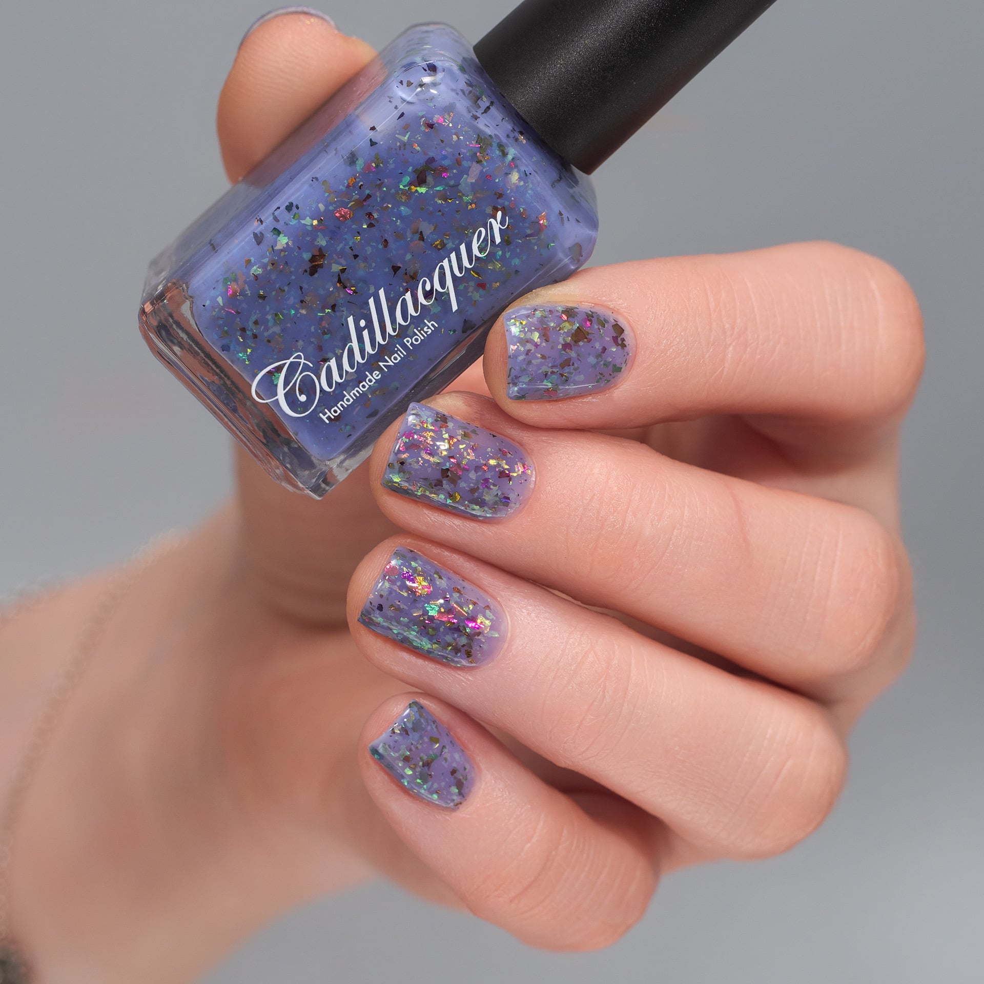 Cadillacquer Don't Worry purple pink chameleon iridescent crelly nail polish, bottle held with four-nail swatch, light skin, studio lighting