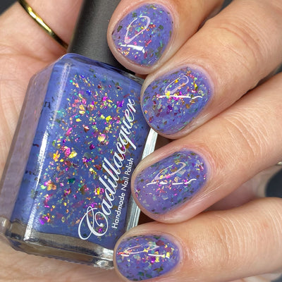 Cadillacquer Don't Worry purple pink chameleon iridescent crelly nail polish, bottle held with four-nail swatch, light skin, studio lighting