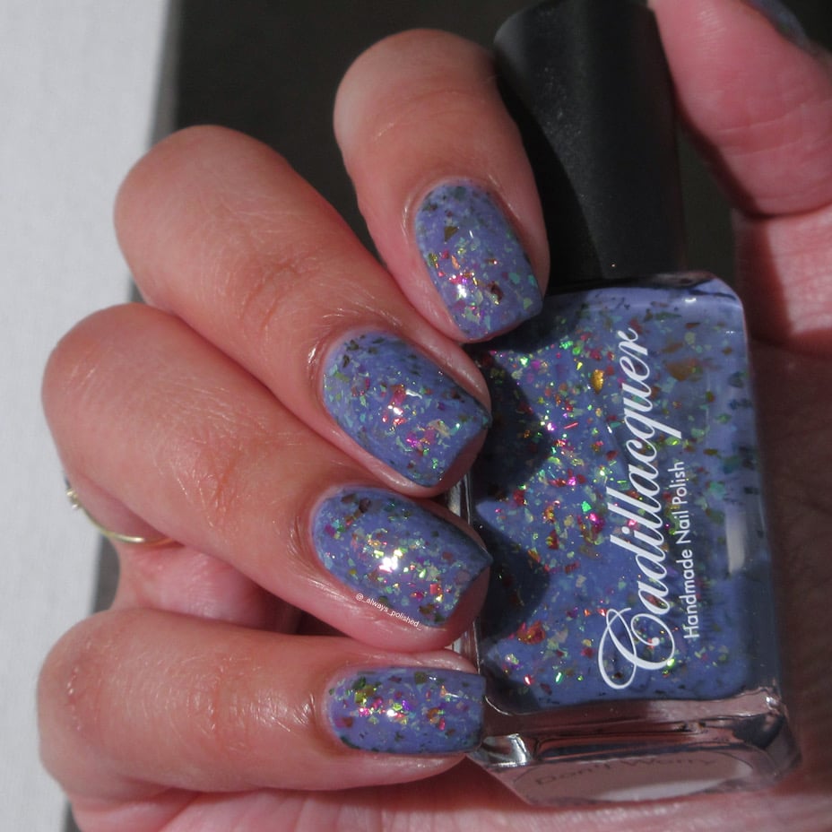 Cadillacquer Don't Worry purple pink chameleon iridescent crelly nail polish, bottle held with five-nail swatch, light skin, bright daylight lighting