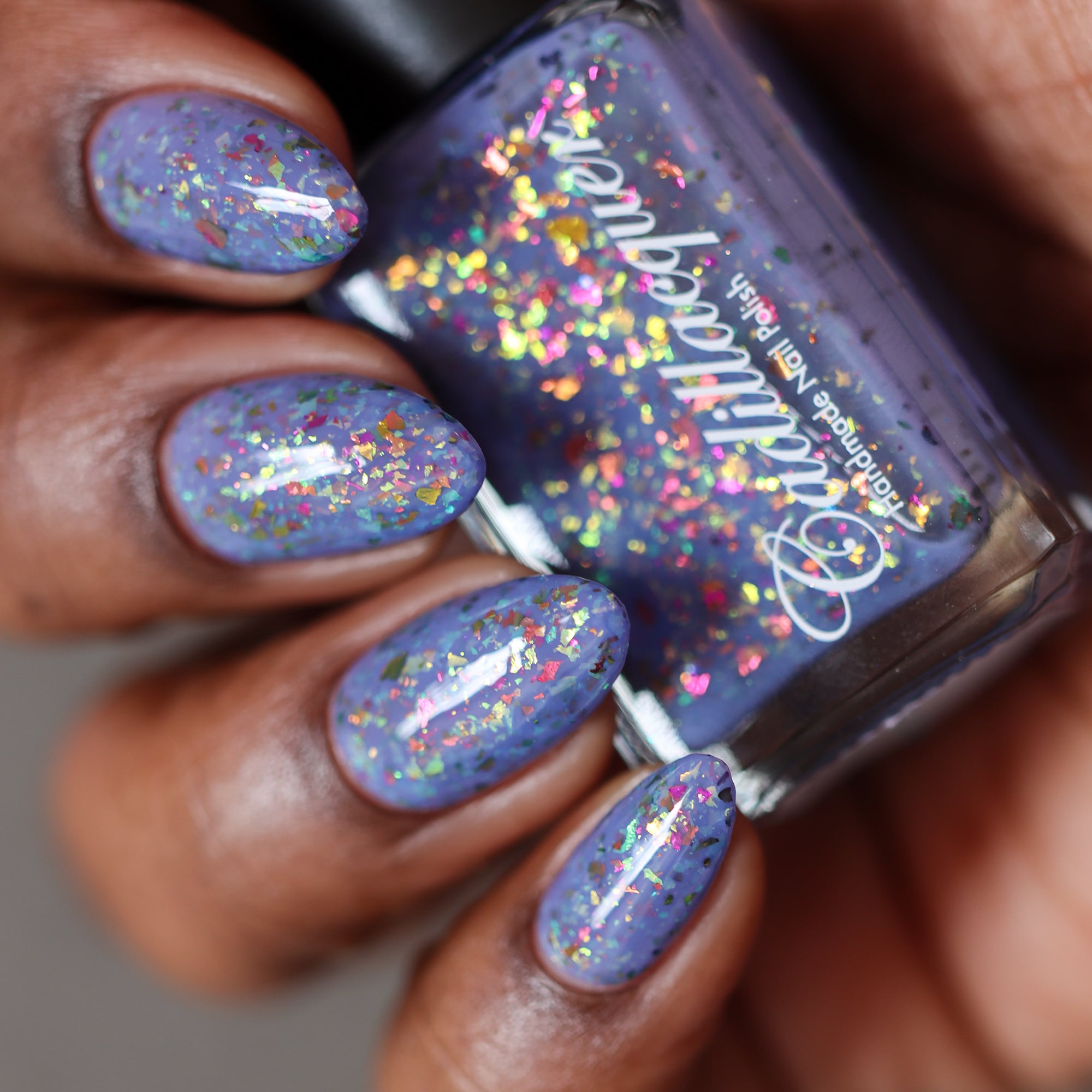 Cadillacquer Don't Worry purple pink chameleon iridescent crelly nail polish, bottle held with four-nail swatch, rich skin, studio lighting