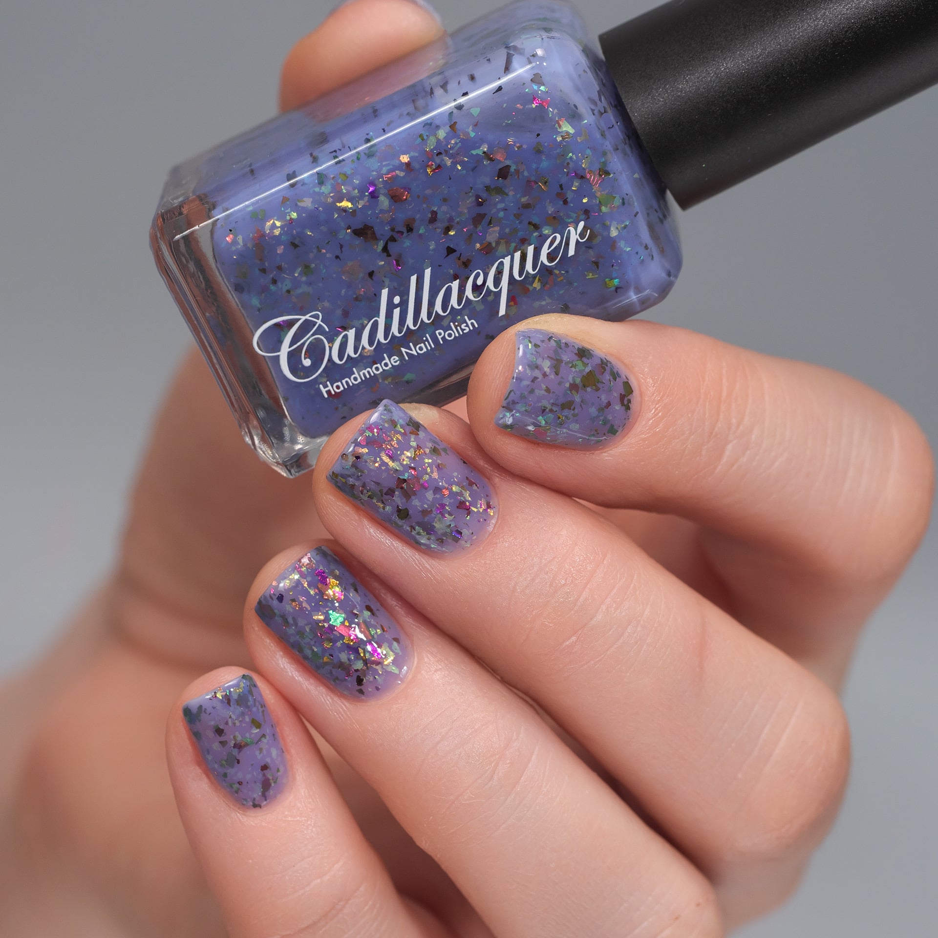 Cadillacquer Don't Worry purple pink chameleon iridescent crelly nail polish, bottle held with four-nail swatch, light skin, studio lighting