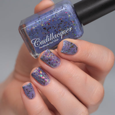 Cadillacquer Don't Worry purple pink chameleon iridescent crelly nail polish, bottle held with four-nail swatch, light skin, studio lighting