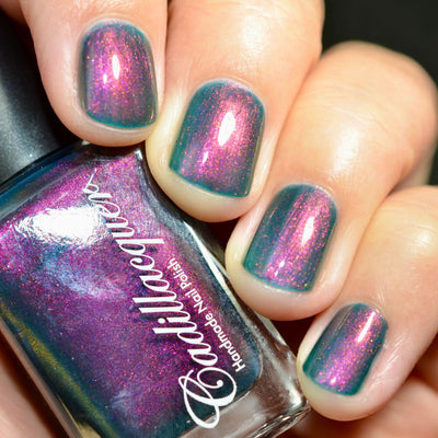 Multichrome shimmer Cadillacquer nail polish in Fear What You Will Become, bottle held in hand beside four swatched squoval nails shifting from murky teal base through magenta to orange shimmer, light skin tone, studio lighting, swatched by @caitlinswatches