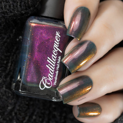 Multichrome shimmer Cadillacquer nail polish in Fear What You Will Become, showing a dark bottle with deep magenta-to-orange shimmer alongside five oval nails on light skin reading murky teal-grey base with a dramatic shift through amber-orange, dusty rose, and magenta shimmer depending on angle, shot under studio lighting, swatched by @serpentine13