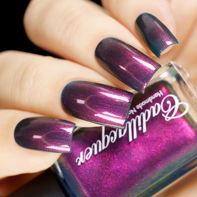 Multichrome shimmer Cadillacquer nail polish in Fear What You Will Become, shown in-hand with four square nails displaying a deep dark plum-teal base packed with magenta-to-orange shimmer that shifts to vivid magenta at high angles and teal at the nail edges, bottle face reads vivid magenta-pink while the bottle rim reveals the true murky teal base, light skin tone, studio lighting, swatched by @yyulia_m