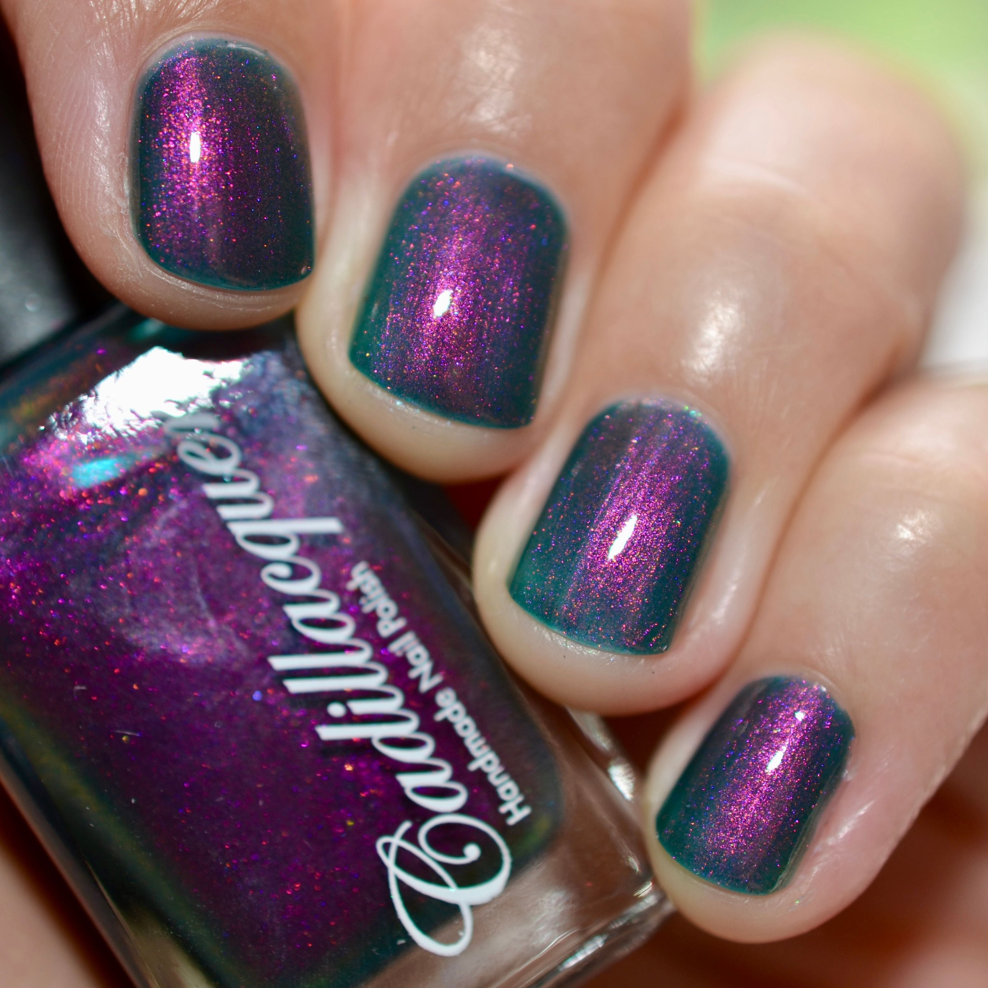Multichrome shimmer Cadillacquer nail polish in Fear What You Will Become, showing bottle in hand alongside four swatched nails, the teal base shifts from magenta to orange with angle, light skin tone, bright daylight lighting, swatched by @caitlinswatches
