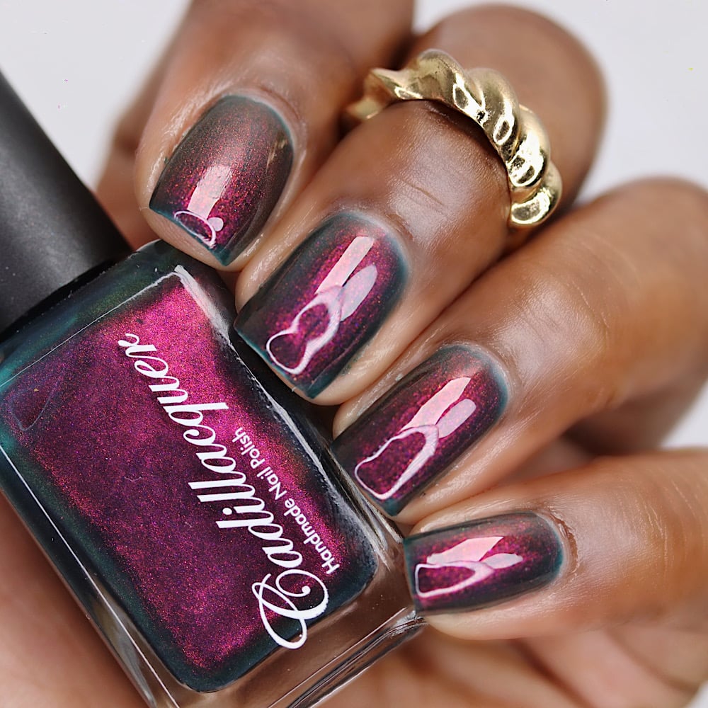 Multichrome shimmer Cadillacquer nail polish in Fear What You Will Become, shown swatched on eight short natural nails with a bottle held in hand, the polish shifts from dark murky teal at the nail edges to vivid magenta-raspberry shimmer at the center under studio lighting, worn on deep skin tone with a gold sculptural ring accent, swatched by @lacquer_is_life