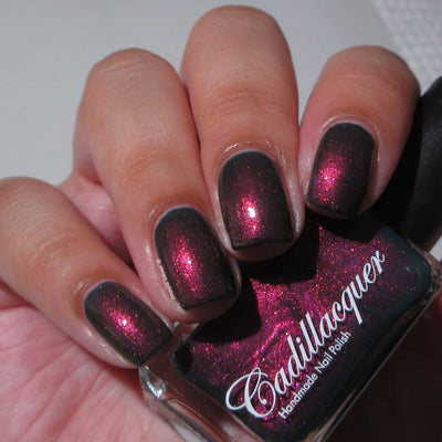 Shimmer Cadillacquer nail polish in Fear What You Will Become, swatched on four square nails held alongside the bottle, showing a near-black base packed with vivid magenta-pink shimmer flash, light skin tone, indoor warm lighting, swatched by @_always_polished_
