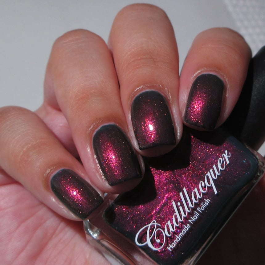 Shimmer Cadillacquer nail polish in Fear What You Will Become, swatched on four square nails held alongside the bottle, showing a near-black base packed with vivid magenta-pink shimmer flash, light skin tone, indoor warm lighting, swatched by @_always_polished_