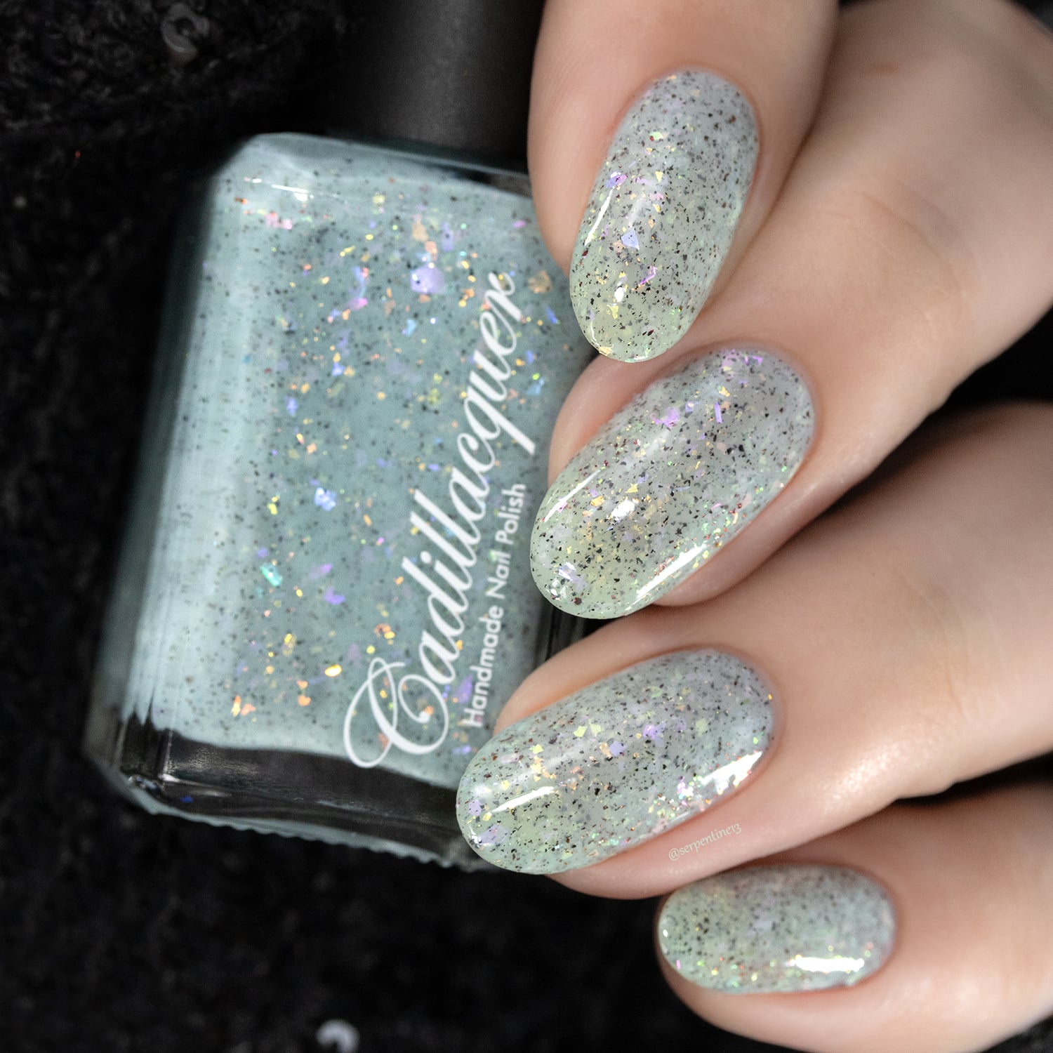 Cadillacquer Fresh Sheets pastel mint iridescent crelly nail polish, bottle held with four-nail swatch, light skin, studio lighting