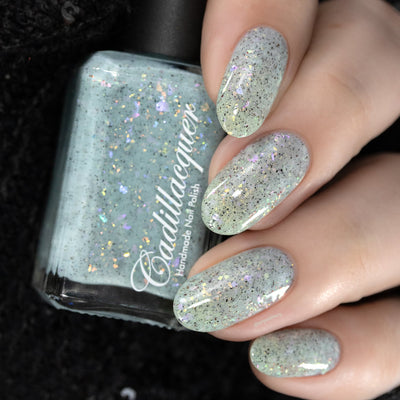 Cadillacquer Fresh Sheets pastel mint iridescent crelly nail polish, bottle held with four-nail swatch, light skin, studio lighting