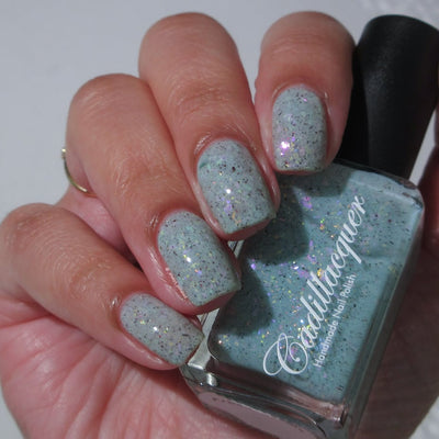 Cadillacquer Fresh Sheets pastel mint iridescent crelly nail polish, bottle held with four-nail swatch, light-medium skin, bright daylight lighting