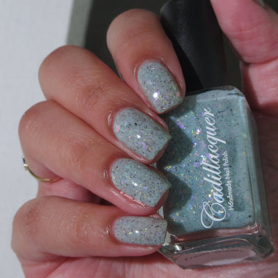 Cadillacquer Fresh Sheets pastel mint iridescent crelly nail polish, bottle held with four-nail swatch, light-medium skin, bright daylight lighting