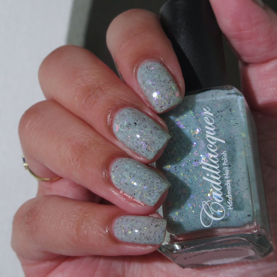 Cadillacquer Fresh Sheets pastel mint iridescent crelly nail polish, bottle held with four-nail swatch, light-medium skin, bright daylight lighting