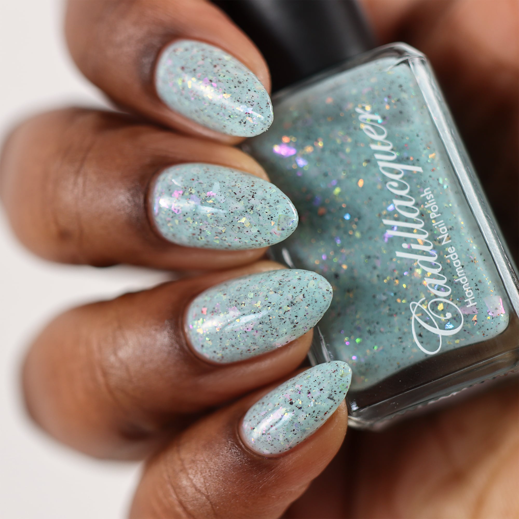 Cadillacquer Fresh Sheets pastel mint iridescent crelly nail polish, bottle held with four-nail swatch, rich skin, studio lighting