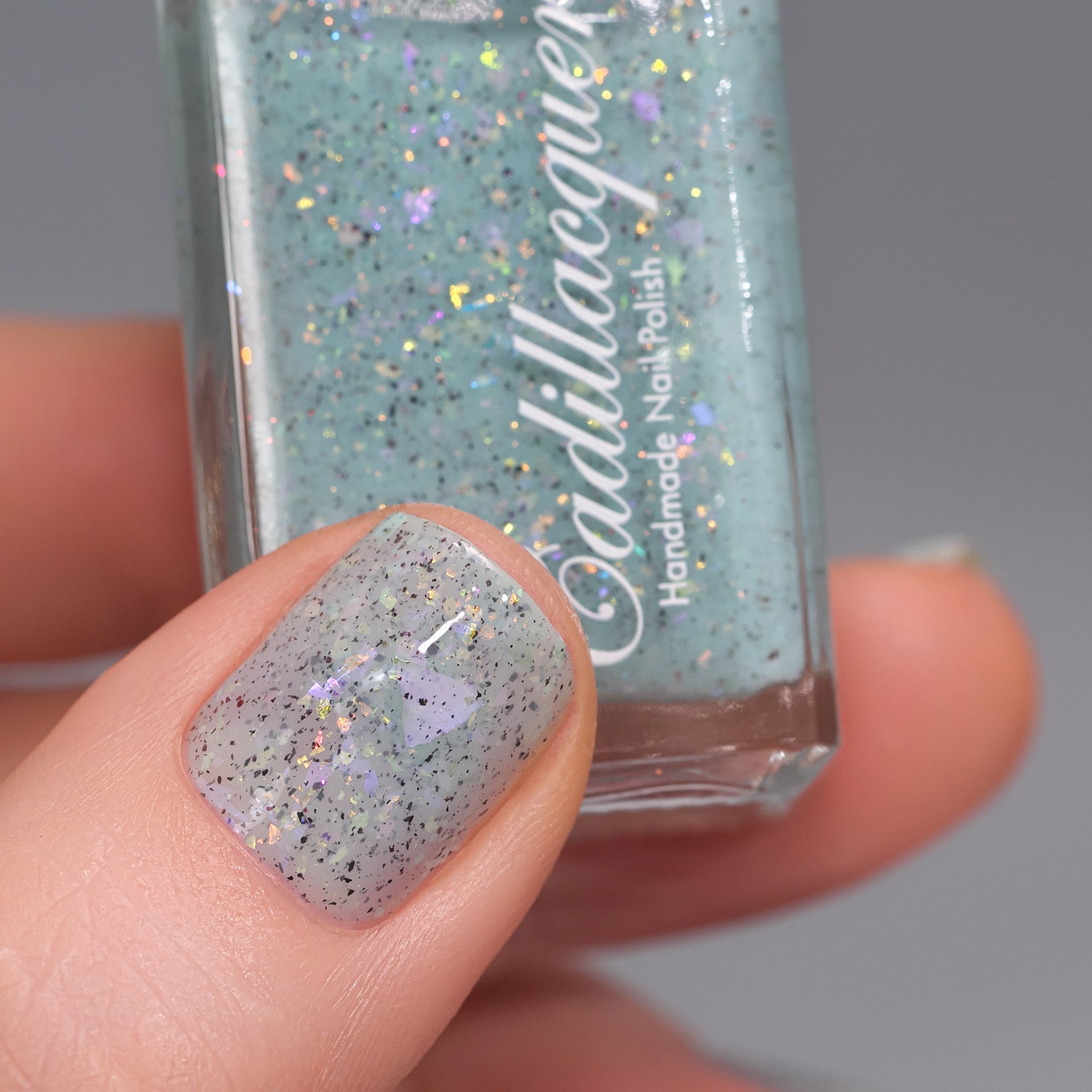 Cadillacquer Fresh Sheets pastel mint iridescent crelly nail polish, bottle held with one-nail swatch, light skin, studio lighting
