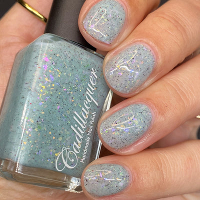 Cadillacquer Fresh Sheets pastel mint iridescent crelly nail polish, bottle held with four-nail swatch, light skin, studio lighting