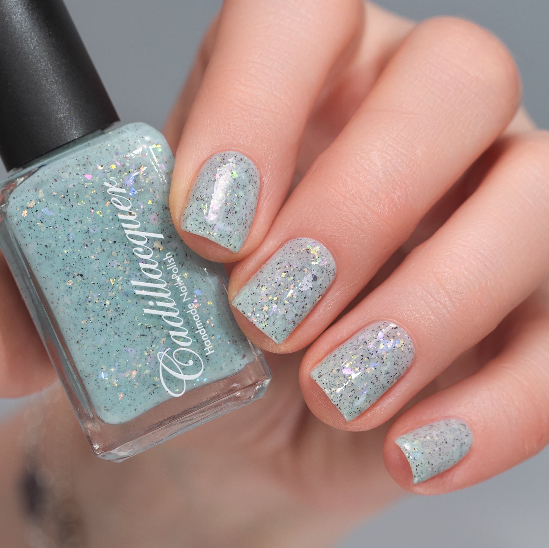 Cadillacquer Fresh Sheets pastel mint iridescent crelly nail polish, bottle held with four-nail swatch, light skin, studio lighting