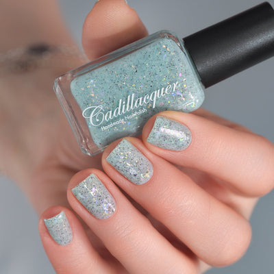 Cadillacquer Fresh Sheets pastel mint iridescent crelly nail polish, bottle held with four-nail swatch, light skin, studio lighting